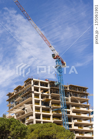 Construction crane above residential building under blue sky. Urban infrastructure, civil engineering, and real estate development 135061901