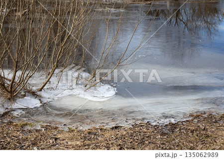 Ice crust on the bank of a frozen river in winter. River in water flows under frozen ice. 135062989