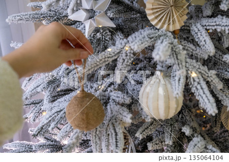 Decorating Snowy Christmas Tree with Ornaments 135064104