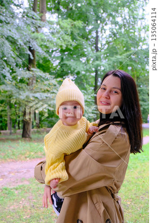 Mother Holding Baby in Yellow Outfit at Park 135064114