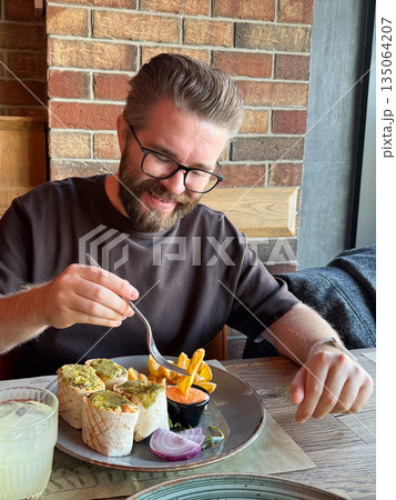 Man enjoying lunch in a restaurant by the window. Warm atmosphere, everyday pleasure and authentic moment of happiness and taste. Man enjoying lunch in a restaurant by the window. Warm atmosphere, everyday pleasure and authentic moment of happiness and taste. 135064207