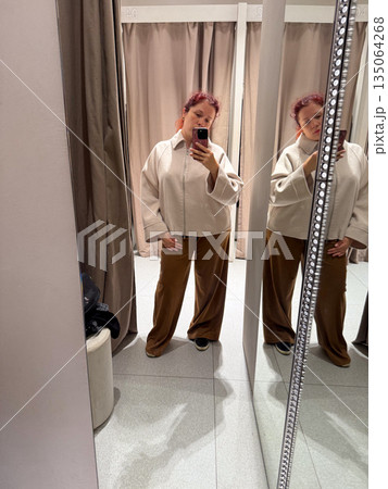 Woman adjusting jacket in fitting room. Exploration of texture, self-awareness, and identity through tactile perception of fashion and minimalist elegance. Woman adjusting jacket in fitting room. Exploration of texture, self-awareness, and identity through tactile perception of fashion and minimalist elegance. 135064268