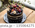 Beautifully decorated chocolate cake topped with fresh fruits and flowers sits on a wooden table in a bright, natural light setting 135064275