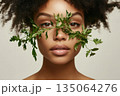 Model showcases natural beauty with green leaves on face against plain background 135064276