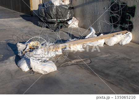 Barbed wire, sandbags and wooden boards blocking a passage and driveway. Temporary barricade and improvised barrier restricting access 135065210