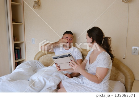 Happy couple enjoying a leisurely morning at home, sipping coffee and engaging with a digital tablet, sharing laughter and deepening their connection in a cozy kitchen setting Happy couple enjoying a leisurely morning at home, sipping coffee and engaging with a digital tablet, sharing laughter and deepening their connection in a cozy kitchen setting 135065371