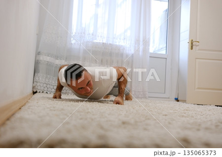 Focused young man doing push-ups outdoors on a concrete path, wearing a grey athletic shirt. Fitness and strength training concept in an urban outdoor setting. Focused young man doing push-ups outdoors on a concrete path, wearing a grey athletic shirt. Fitness and strength training concept in an urban outdoor setting. 135065373