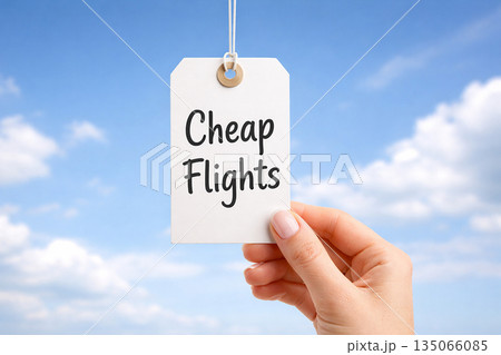 Hands holding a white paper price tag that reads cheap flights against bright blue sky Hands holding a white paper price tag that reads cheap flights against bright blue sky 135066085