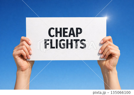 Hands holding a white paper sign that reads cheap flights against bright blue sky and sun flare 135066100