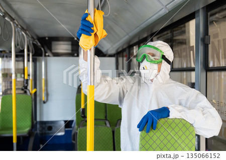 Workers in full protective hazmat suits perform thorough antiviral and antibacterial disinfection inside a public bus Workers in full protective hazmat suits perform thorough antiviral and antibacterial disinfection inside a public bus 135066152