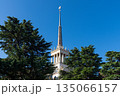 A striking view of the elegant spire of Sochi's Maritime Station piercing the sky, captured through the vibrant green foliage of overhanging tree branches. 135066157