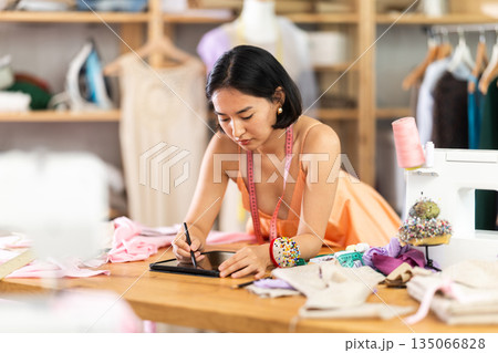 Young woman drawing sketch on tablet in sewing workshop 135066828