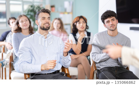 Young guy commenting during lesson in modern classroom Young guy commenting during lesson in modern classroom 135066862
