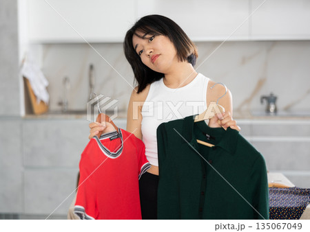 Sad young Asian girl trying to choose a dress in the kitchen Sad young Asian girl trying to choose a dress in the kitchen 135067049