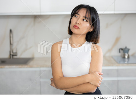 Sad young Asian girl standing at table in the kitchen 135067080