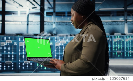 Developer in data center using green screen laptop to upgrade systems for increased stability. IT expert in server farm configuring hardware with mockup notebook for optimum performance, camera A Developer in data center using green screen laptop to upgrade systems for increased stability. IT expert in server farm configuring hardware with mockup notebook for optimum performance, camera A 135067634