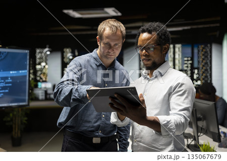 Team of programmers in office doing brainstorming, automating repetitive tasks using AI scripts on devices. Colleagues work together using artificial intelligence to speed up feature implementation 135067679