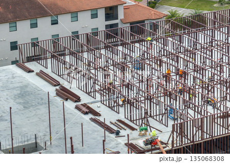 Construction works on metal walls of commercial building. Blue collar workers at large site with scattered equipment. Development of residential housing in America. Real estate market in USA 135068308