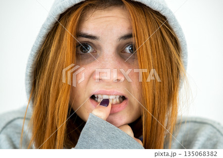 Close up portrait of scared young redhead woman wearing warm hoodie pullover. Close up portrait of scared young redhead woman wearing warm hoodie pullover. 135068382