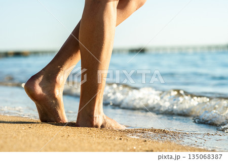 Close up of woman feet walking barefoot on sand beach in sea water. Vacation, travel and freedom concept. People relaxing in summer. Close up of woman feet walking barefoot on sand beach in sea water. Vacation, travel and freedom concept. People relaxing in summer. 135068387