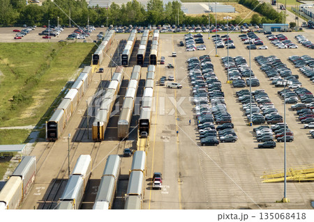 Cargo train transporting cars. Factory parking lot with many brand new cars for sale. Development of American automotive industry concept 135068418