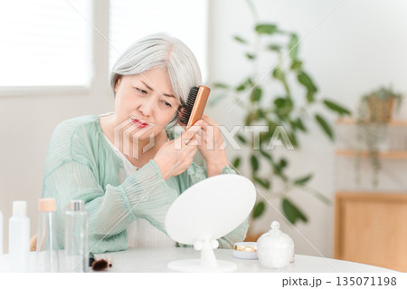 自宅のリビングで鏡を見ながらヘアケアするグレイヘアのシニアのアジア人女性(困る,悩む,悩み) 自宅のリビングで鏡を見ながらヘアケアするグレイヘアのシニアのアジア人女性(困る,悩む,悩み) 135071198