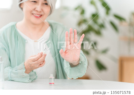 爪にマニキュア・ネイルオイルを塗って保湿するグレイヘアーのシニア女性 爪にマニキュア・ネイルオイルを塗って保湿するグレイヘアーのシニア女性 135071578