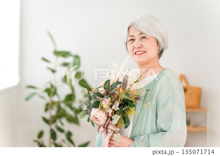 自宅のリビングで花束を持つグレイヘアーのシニア女性 135071714