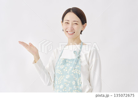 左側を手のひらで指すエプロンをつけた女性 白背景 左側を手のひらで指すエプロンをつけた女性 白背景 135072675