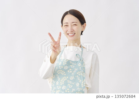 エプロンをつけた女性　ピースサイン　白背景 135072684