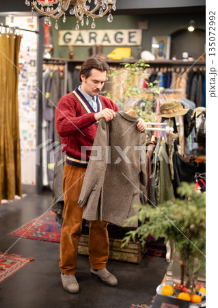 Fashionable man buying trendy old fashioned jacket in second hand store, sustainable fashion. 135072992
