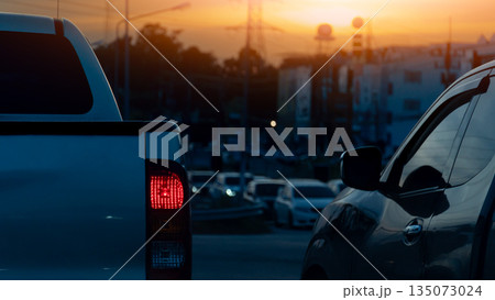 Rear side of pickup car with turn on brake light in dark tone. Environment traffic jams on the junction with many cars. Background of city and forest under light of evening sky. 135073024