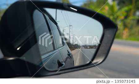 Car side mirror view reflecting the asphalt road and blue sky. Transportation, travel, and driving safety concept. Traffic conditions are clear. with electric pole side of road in Thailand. Car side mirror view reflecting the asphalt road and blue sky. Transportation, travel, and driving safety concept. Traffic conditions are clear. with electric pole side of road in Thailand. 135073145