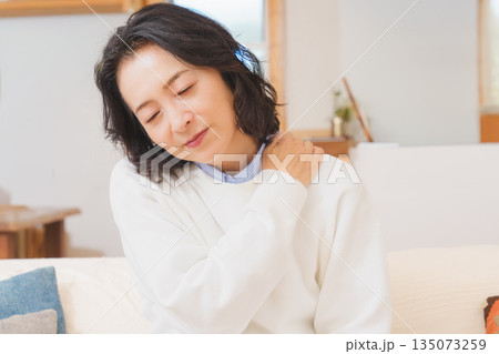 リビングでソファに座り肩をもむミドル女性 135073259
