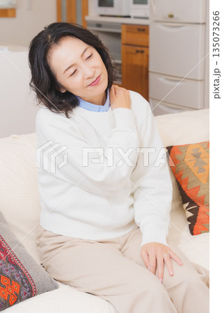 リビングでソファに座り肩をもむミドル女性 135073266