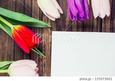Flat design is showing blank white paper on dark wood tabletop, with colorful tulips 135073681