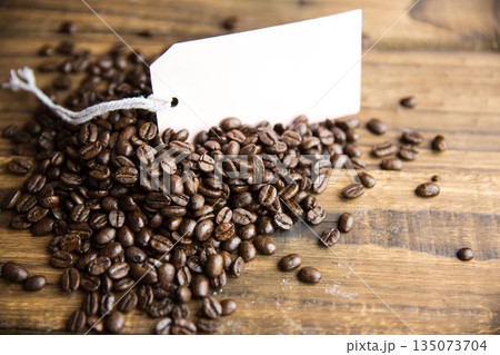 Flat design roasted coffee beans pile is being shown on wooden table, with blank white tag 135073704