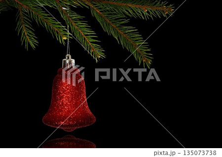 Red glitter bell ornament is hanging from pine branch in 3D with silver cap, black backdrop 135073738