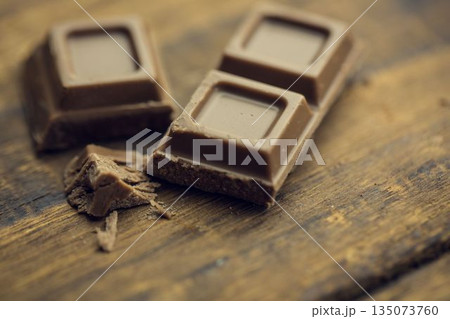 Flat design milk chocolate squares are resting on wooden surface with scattered shavings and crumbs Flat design milk chocolate squares are resting on wooden surface with scattered shavings and crumbs 135073760