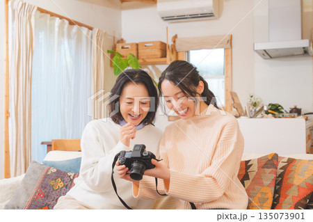 リビングで写真を見ながら旅行の思い出を楽しく話す母と娘 135073901