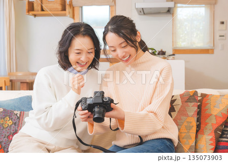 リビングで写真を見ながら旅行の思い出を楽しく話す母と娘 リビングで写真を見ながら旅行の思い出を楽しく話す母と娘 135073903