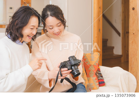 リビングで写真を見ながら旅行の思い出を楽しく話す母と娘 135073906