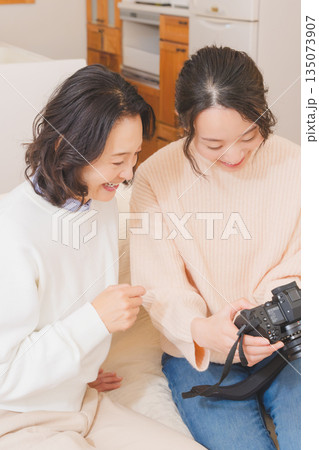 リビングで写真を見ながら旅行の思い出を楽しく話す母と娘 リビングで写真を見ながら旅行の思い出を楽しく話す母と娘 135073907