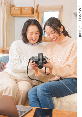 リビングで写真を見ながら旅行の思い出を楽しく話す母と娘 135073911