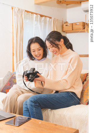 リビングで写真を見ながら旅行の思い出を楽しく話す母と娘 135073912