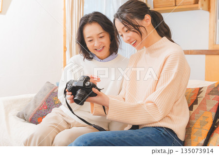 リビングで写真を見ながら旅行の思い出を楽しく話す母と娘 リビングで写真を見ながら旅行の思い出を楽しく話す母と娘 135073914