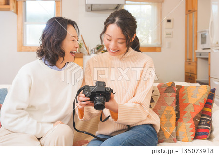 リビングで写真を見ながら旅行の思い出を楽しく話す母と娘 リビングで写真を見ながら旅行の思い出を楽しく話す母と娘 135073918