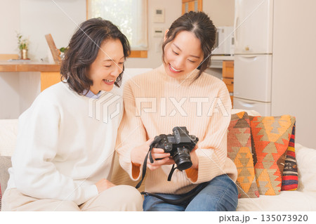リビングで写真を見ながら旅行の思い出を楽しく話す母と娘 リビングで写真を見ながら旅行の思い出を楽しく話す母と娘 135073920
