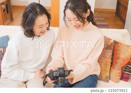 リビングで写真を見ながら旅行の思い出を楽しく話す母と娘 135073921