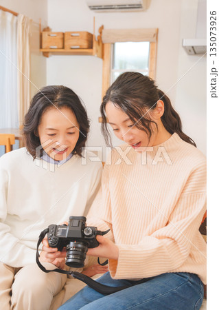 リビングで写真を見ながら旅行の思い出を楽しく話す母と娘 リビングで写真を見ながら旅行の思い出を楽しく話す母と娘 135073926